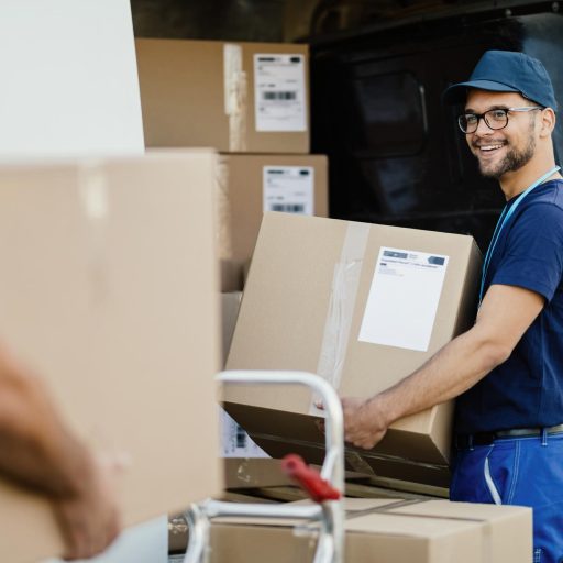 Young happy manual worker carrying cardboard boxes in delivery van while